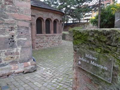 Skylt till mikvan (rituellt bad) och Judiska museet, inrymt i Raschi-huset bakom synagogan. Till höger (den låga delen av synagogan): Raschi-jeschivan.